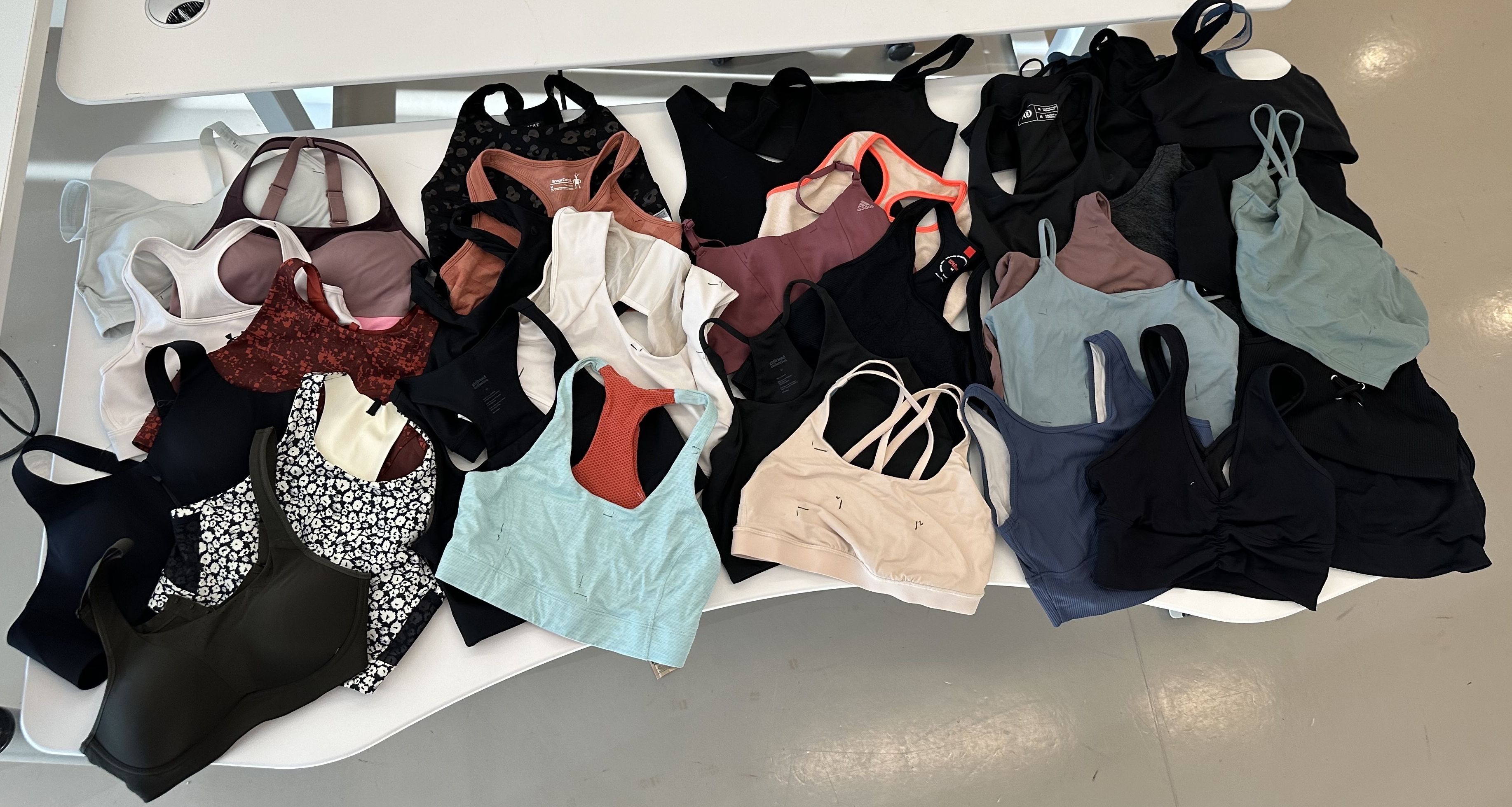 a variety of sports bras spread out on a white table, good housekeeping's testing for the best sports bras